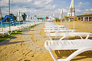 Golden sand and white beach chairs with umbrella around the big swimming pool in Strand Ostroveni from Ramnicu Valcea. Romania -