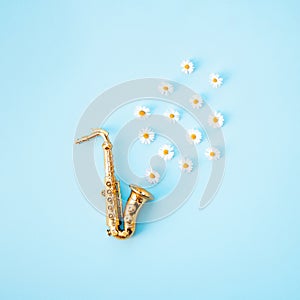 A golden saxophone from which Shasta daisy flowers hatch. Minimal concept on a light blue background