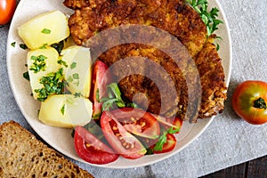 Golden schnitzel, boiled potatoes and salad with tomatoes on a plate