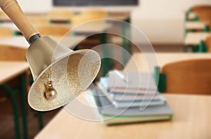 Golden school bell with wooden handle and blurred view of books on desk in classroom