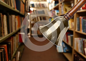 Golden school bell with wooden handle and blurred view of books on shelves in library