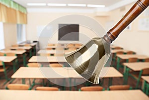 Golden school bell with wooden handle and blurred view of empty classroom