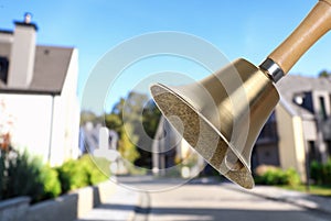 Golden school bell with wooden handle and blurred view of street on sunny day