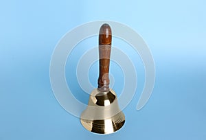 Golden school bell with wooden handle on light blue background