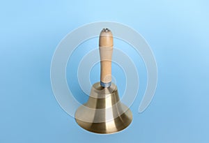 Golden school bell with wooden handle on light blue background