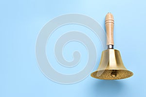 Golden school bell with wooden handle on light blue background, top view. Space for text