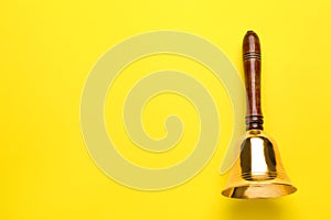 Golden school bell with wooden handle on yellow background, top view. Space for text