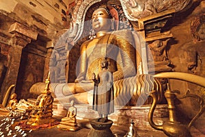 Golden sculpture of meditating Buddha inside cave of stone temple. Buddhist structure with sculptures, Sri Lanka