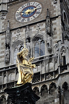 Golden scuplture of Virgin Mary at  clock tower Marienplatz under blue sky backgrounds, Munich, Germany, Travel photo