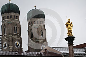 Golden scuplture of Virgin Mary at  Marienplatz with Both onion domes of the Gothic cathedral backgrounds, Munich, Germany