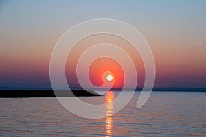 Golden setting sun over the sea just above horizon with optic straight line of light reflection on water surface