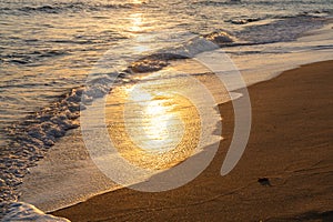 Golden shimmering sunset light on gentle waves on a sandy beach