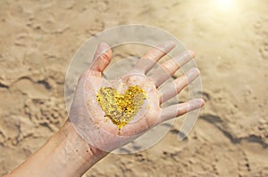 A golden shining heart lies in the hands of the girl. Heart in the palms. Golden heart