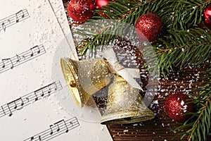 Golden shiny bells with bow, music sheet and red decorative balls on wooden table, flat lay. Christmas decoration