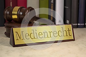 Golden sign with gavel on a desk with the german word for Media Law - Medienrecht