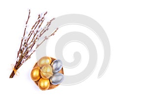 Golden and silver colored Easter eggs on wooden plate with willow catkins branches isolated on white background. Place for text.