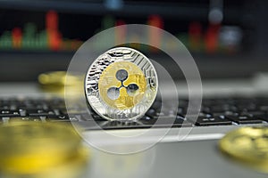 Golden and Silver Ripple coin with gold coins lying around on a black keyboard of silver laptop and diagram chart graph