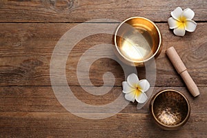 Golden singing bowls, mallet and flowers on wooden table, flat lay. Space for text