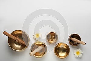 Golden singing bowls, mallets and flowers on white background, flat lay. Space for text