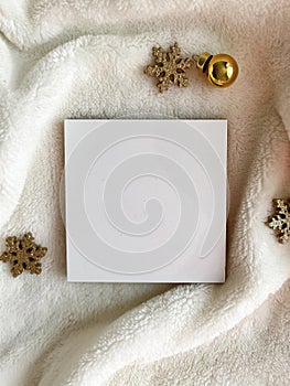 Golden snowflakes and a golden Christmas tree toy lie next to an empty white square on a white fur background.