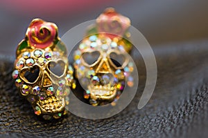 Golden sparkling earrings in the shape of smiling skulls for Helloween party