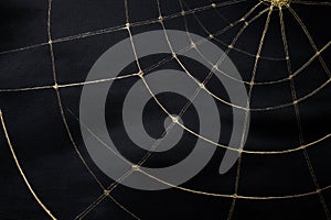 Golden spider web pattern on black fabric background with soft folds and shadows photo