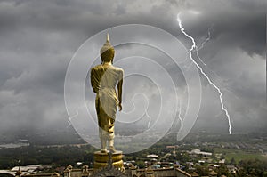 Golden standing Buddha image and lightning storm over the town