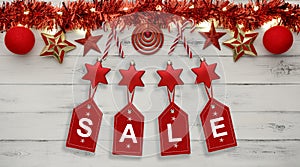 Golden star christmas lights, and christmas baubles, on a destressed white wooden background, above hanging tags spelling sale