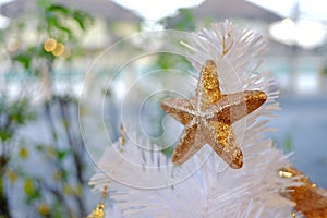 A golden star ornament hanging from a white Christmas tree