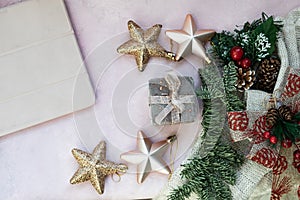 Golden stars, gift box, christmas tree branch and decorations on light pink textured background.