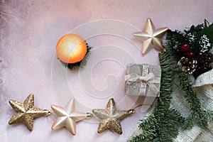 Golden stars, gift box, christmas tree branch and decorations on light pink textured background.