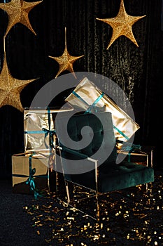 Golden stars hanging on a dark background, New Year's gifts in gold wrappers, a green chair on a dark background