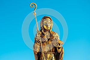 Golden statue of Saint Walpurga before a blue background - Anglo-Saxon missionary sculpture