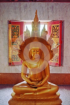 Golden statue of a sitting Buddha protected by Naga serpents