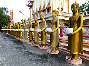 Golden statues of monks holding white alms bowl stand around the ordination hall
