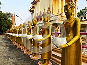 Golden statues of monks holding white alms bowl stand around the ordination hall