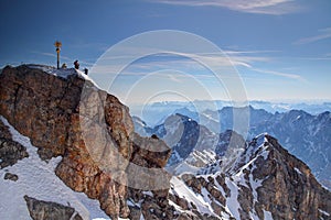 Golden summit cross and tiny climbers on top of Zugspitze peak