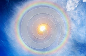 Golden sun on blue sky background with many flames and huge rainbow halo at noon