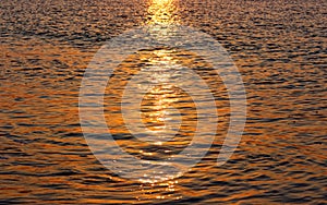 Golden sun glitter on rippled water surface of ocean by sunset