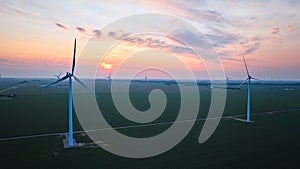 Golden sun at sunset in pink and purple sky over wind farm in farmland aerial