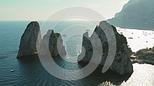 Golden sunlight over Capri and its Faraglioni rocks, yachts cruising past. Warm landscape, inviting onlookers to its