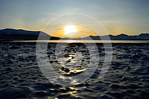 Golden sunrise over blue fjord and snowy mountain with reflection on thick frozen sea shore ice