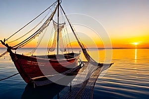 Golden Sunrise Over Ocean: Weathered Fishing Boat with Nets Navigating Calm Sea Waters