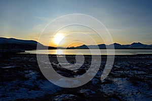 Golden sunrise over blue fjord and snowy mountain with reflection on thick ice