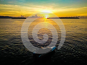 Golden sunrise and a speed boat on calm sea water with background of two islands in Talaud, north Sulawesi, Indonesia