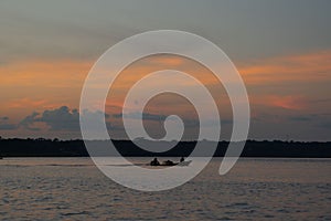 Golden sunset on calm Amazon river. Kayak with unrecognizable fishermen