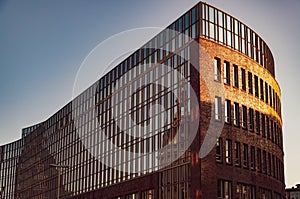 Low angle view to modern bank building with glass wall and abstract reflection in sunset golden sunlight