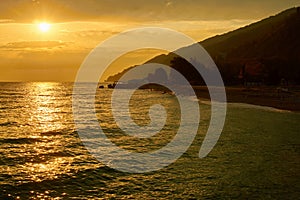 Golden sunset over sea with clouds, mountain and beach in backlight