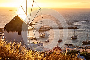 Golden sunset over sea horizon in Mykonos, Greece. Famous traditional white windmill on hot summer evening in sunlight