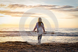 Golden sunset over sea with silhouette cute girl child on holiday vacation evening looking to horizon rising setting sun